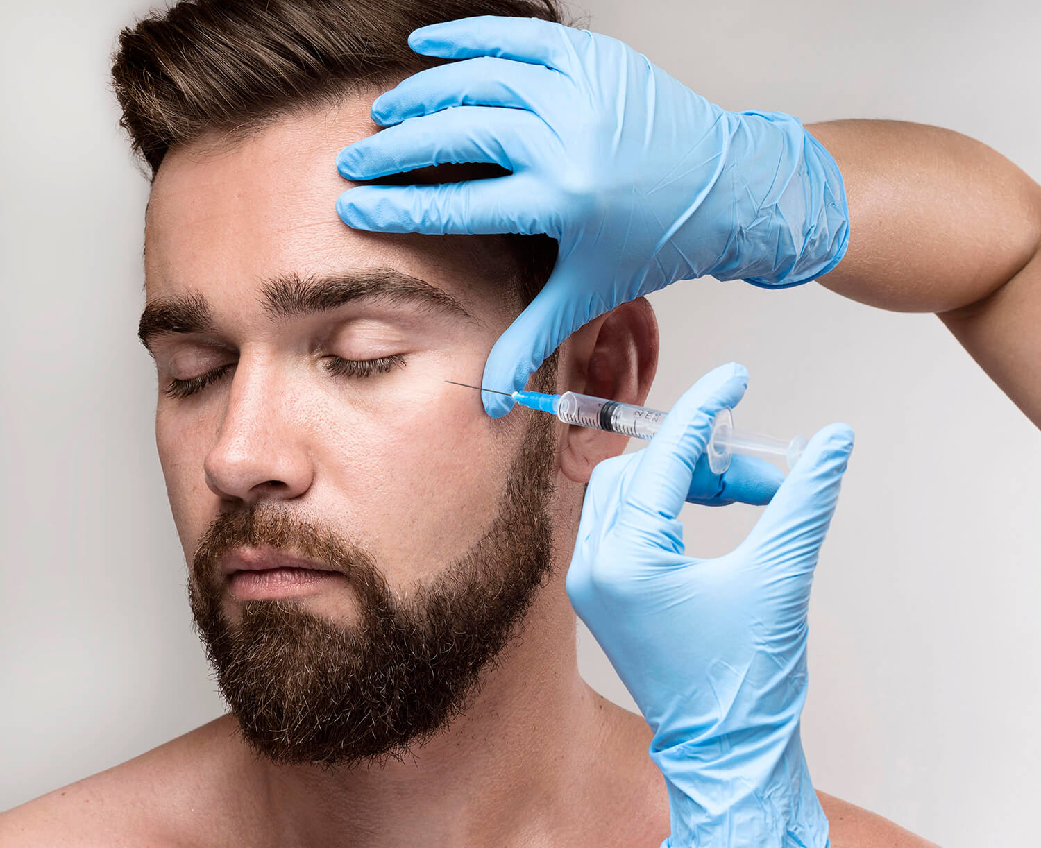 Manos con guantes azules pinchando una aguja en las ojeras de un hombre