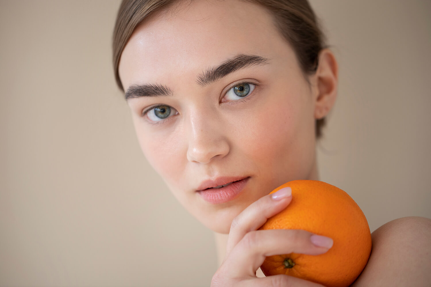 Rostro de una mujer mirando a cámara sosteniendo una naranja en su hombro